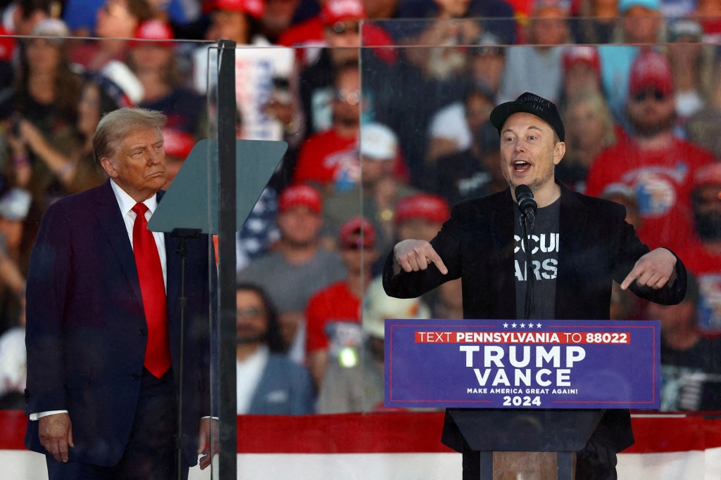 Tesla CEO Elon Musk speaking at Trump rally while Trump looks on.